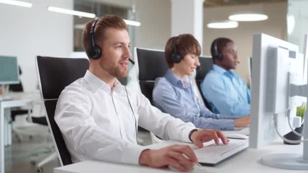 Group of multiethnic operators with headset sitting at desk. Focused answering incoming calls from customers. Working on computers and typing texts on keyboards. Concept of business service. - Footage, Video