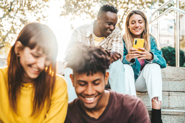 Multicultural millennial personas utilizando el dispositivo de teléfono móvil inteligente sentado al aire libre - Foto, imagen
