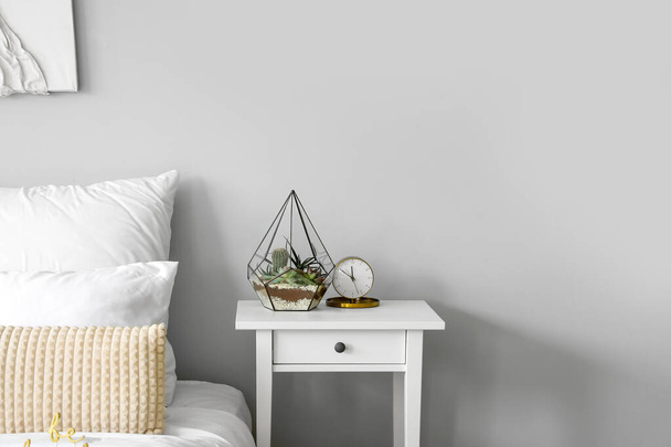 Florario con reloj despertador en mesa en dormitorio luminoso - Foto, imagen