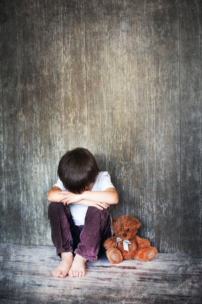 Νεαρό αγόρι, κάθεται στο πάτωμα, αρκουδάκι δίπλα του, το κλάμα - Φωτογραφία, εικόνα