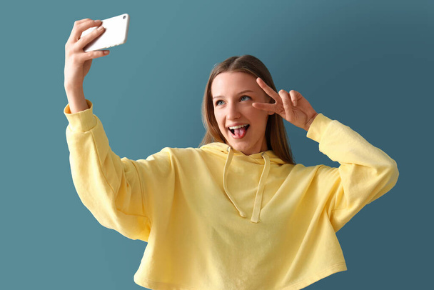 Teenage girl with mobile phone taking selfie on blue background - Photo, Image