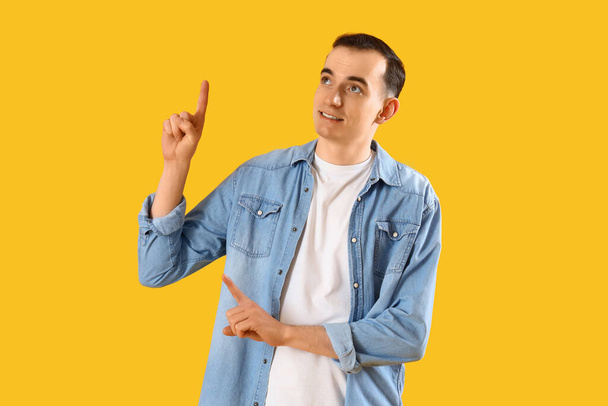 Young man pointing at something on yellow background - Photo, Image