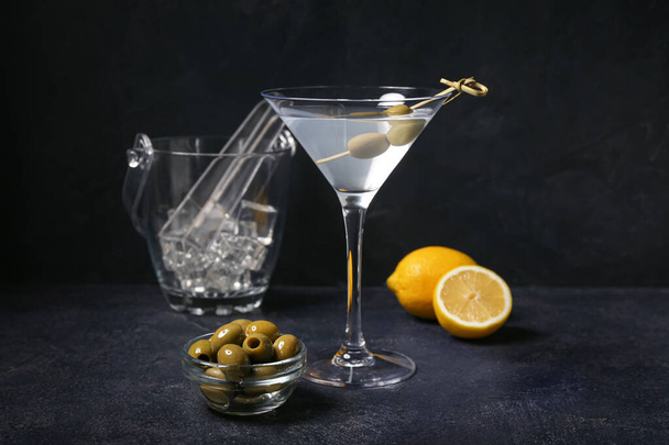 Bicchiere di gustosi martini, limone, cubetti di ghiaccio e olive verdi su fondo scuro - Foto, immagini