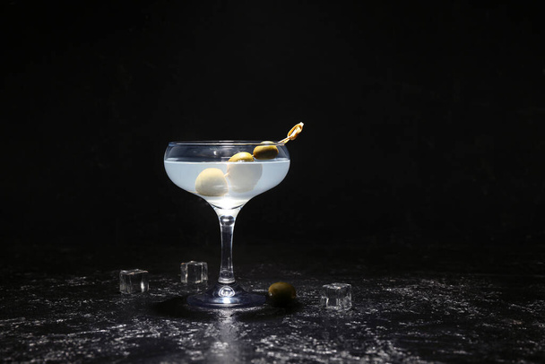 Glas leckerer Martini mit Oliven und Eiswürfeln auf dunklem Hintergrund - Foto, Bild