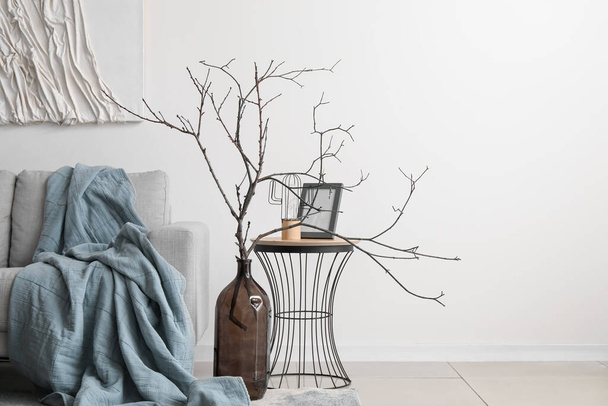 Interior of cozy living room with grey sofa tree branches in vase near white wall - Photo, Image