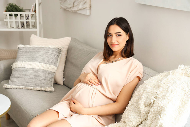 Junge schwangere Frau sitzt zu Hause auf Sofa - Foto, Bild