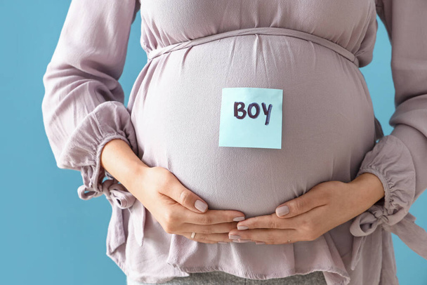 Giovane donna incinta e carta con la parola BOY sulla pancia sullo sfondo blu, primo piano - Foto, immagini