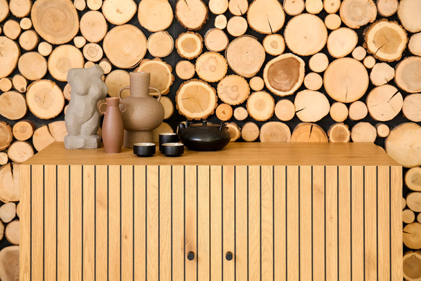 Teapot with cups and decor on chest of drawers near wooden wall - Fotoğraf, Görsel