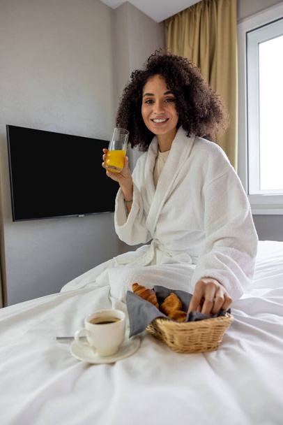 Breakfast in the hotel. Cute young woman in white bath robe having breakfast - Фото, изображение