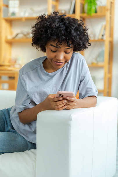 Akıllı telefon tutan Afrikalı bir kız. Evde parşömen sayfasına dokunuyor. Sosyal medya uygulamaları kullanarak internette cep telefonu sörfü yapan bir kadın. İnternet üzerinden haber alışverişi cep telefonu bağımlılığı - Fotoğraf, Görsel