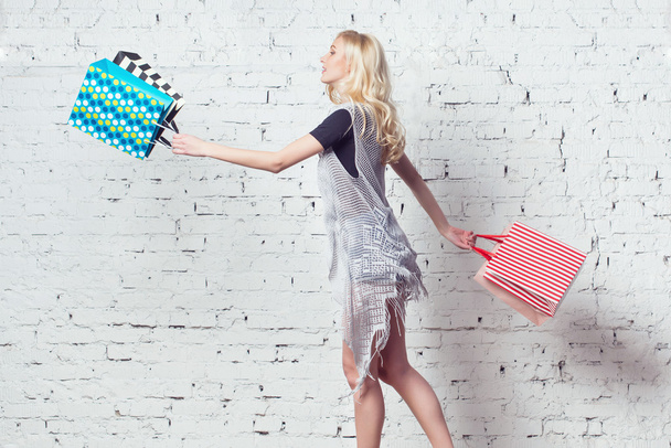 Amazing blond girl is going shopping with couple of colorful bags in her hands. - Photo, Image