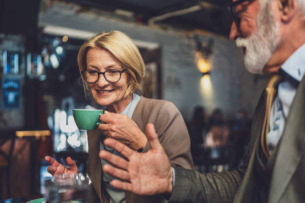 dojrzała kobieta i starszy mężczyzna para angażują się w rozmowę podczas filiżanki ciepła kawy i koleżeństwa rozkoszować się prostą przyjemność dobrego towarzystwa tworząc wspomnienia w otoczeniu kawiarni - Zdjęcie, obraz