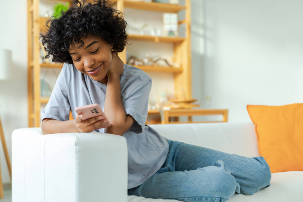 African girl holding smartphone touch screen typing scroll page at home. Woman with cell phone surfing internet using social media apps playing game. Shopping online Internet news cellphone addiction - Zdjęcie, obraz