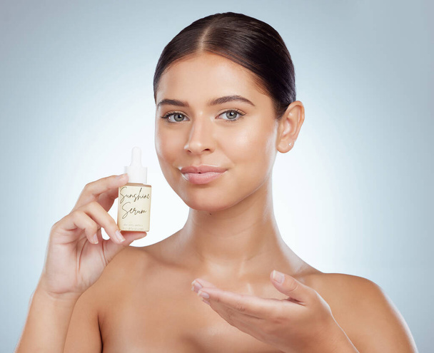 Portrait of beautiful woman holding face serum while posing with copyspace. Young caucasian model isolated against grey studio background. Using skin oil for healthy glowing skin for skincare routine. - Foto, Imagen