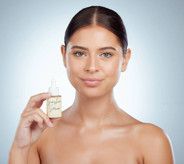 Portrait of beautiful woman holding face serum while posing with copyspace. Young caucasian model isolated against grey studio background. Using skin oil for healthy glowing skin for skincare routine. - Fotoğraf, Görsel