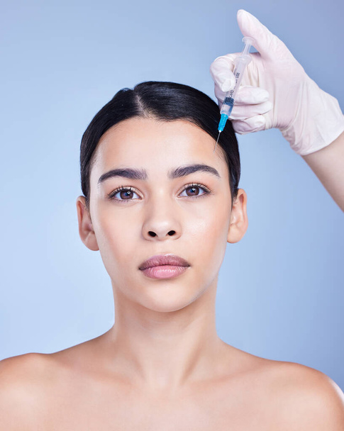 Studio portrait of a gorgeous mixed race woman getting botox filler. Hispanic model getting cosmetic surgery against a blue copyspace background. - 写真・画像