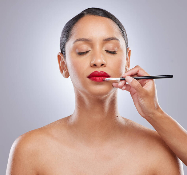 Un labio rojo audaz es mi punto de partida. una atractiva joven mujer de pie en el estudio mientras que un artista de maquillaje aplica lápiz labial - Foto, Imagen