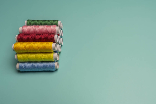 Bobinas de hilo de coser multicolor apiladas sobre una superficie azul turquesa - Foto, imagen
