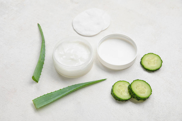 Composition with jar of natural cream, cotton pads, aloe leaves and cucumber slices on light background - Фото, изображение