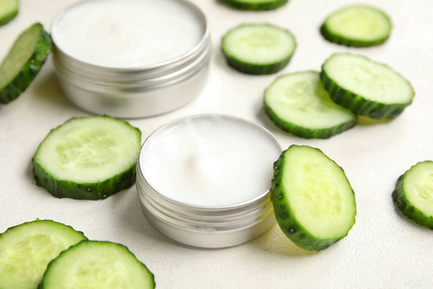 Jars of natural cream and cucumber slices on light background, closeup - Fotó, kép