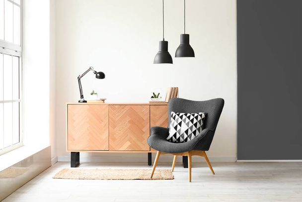 Cozy grey armchair and stylish wooden cabinet near big window - Photo, Image