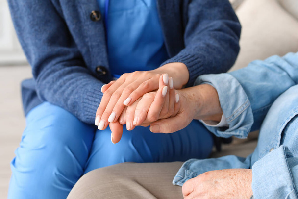 Young caregiver with senior woman holding hands at home, closeup - Foto, Imagem