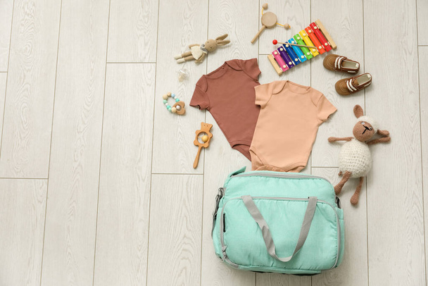 Stilvolle Tasche mit Kleidung und Babyspielzeug auf hellem Holzhintergrund - Foto, Bild