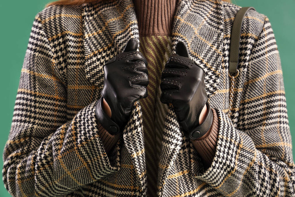 Beautiful woman in leather gloves and coat on green background, closeup - Φωτογραφία, εικόνα