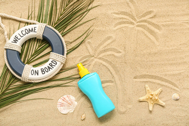 Composición creativa con crema protector solar, salvavidas y hojas de palma sobre arena - Foto, imagen