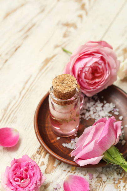 Bottle of cosmetic oil with rose extract and flowers on light wooden table - Foto, Imagem