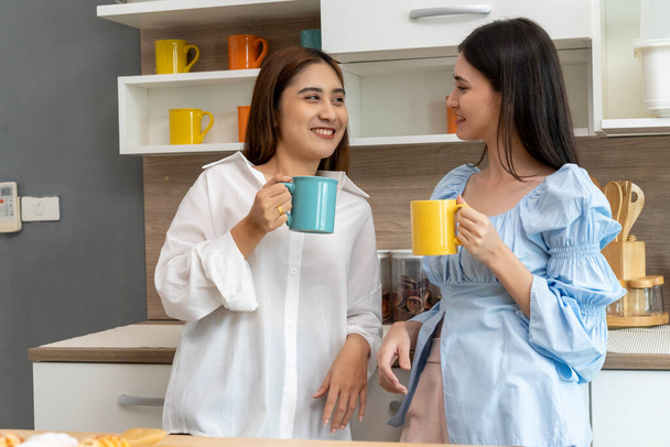 Happy Asian young pretty woman and her girlfriend holding coffee mugs and chatting together in kitchen, The moment romantic time of female lover, LGBTQ freedom of love concept, copy space - Фото, изображение