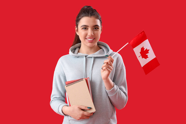 Young woman with flag of Canada and books on red background - Photo, Image
