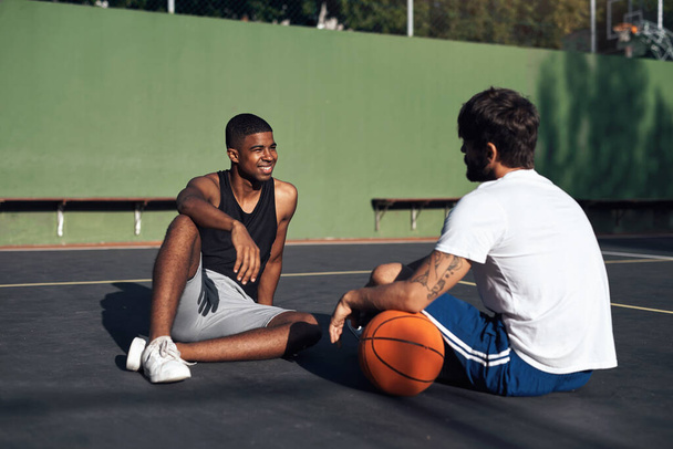 Απλά χαλαρώνω στο γήπεδο. δύο νεαροί αθλητικοί άνδρες που συζητούν μεταξύ τους σε γήπεδο μπάσκετ - Φωτογραφία, εικόνα