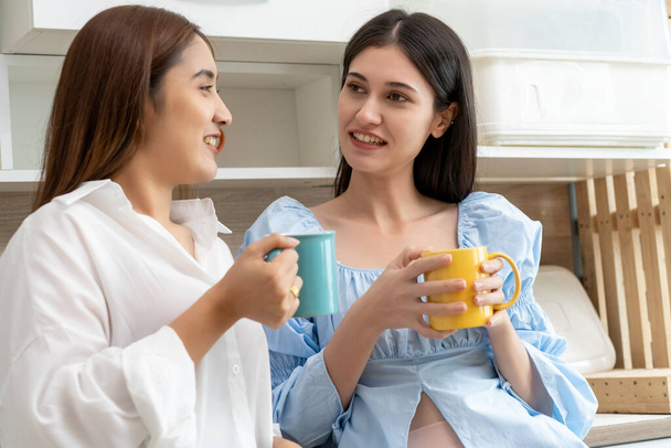 Happy Asian young pretty woman and her girlfriend holding coffee mugs and chatting together in kitchen, The moment romantic time of female lover, LGBTQ freedom of love concept, copy space - Foto, imagen