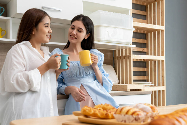Happy Asian young pretty woman and her girlfriend holding coffee mugs and chatting together in kitchen, The moment romantic time of female lover, LGBTQ freedom of love concept, copy space - Foto, Imagen