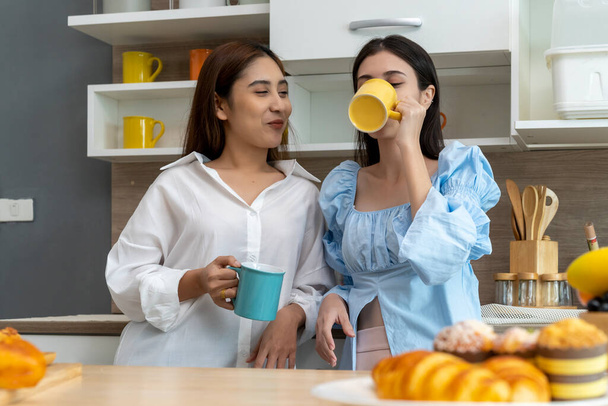 Happy Asian young pretty woman and her girlfriend holding coffee mugs and chatting together in kitchen, The moment romantic time of female lover, LGBTQ freedom of love concept, copy space - Фото, изображение