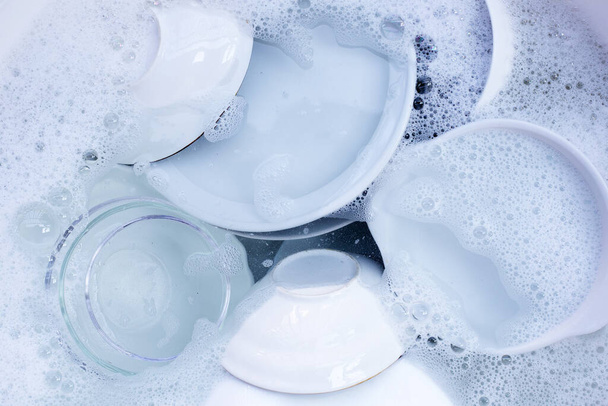 Dishes and bowls in water and bubbles of dishwashing liquid - 写真・画像