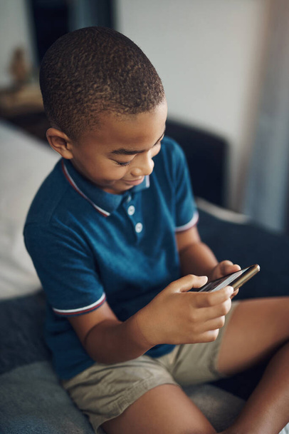 Zijn telefoon is ingesteld op goedkeuring voor het downloaden van een app. een jonge jongen met behulp van een mobiele telefoon tijdens het zitten op zijn bed - Foto, afbeelding