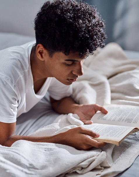 Займись действительно хорошей книгой. молодой человек читает книгу и отдыхает на кровати дома - Фото, изображение