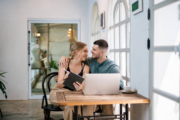 Loving young caucasian couple using laptop together while sitting in chair at home. Concept of couples sharing one idea together. - Photo, Image