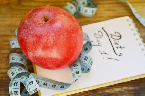 έννοια της διατροφής με κόκκινο μήλο, ένα σημειωματάριο και μπλε μεζούρα στο ξύλινο τραπέζι - Φωτογραφία, εικόνα