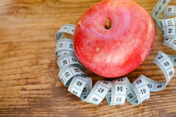 Concepto de dieta con manzana roja y cinta métrica azul en mesa de madera
 - Foto, imagen