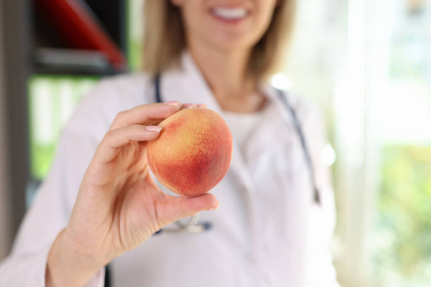 手に熟した桃を保持する医師の栄養士のクローズアップ.健康食品、食事、ビタミン、バランスのとれた栄養の概念 - 写真・画像