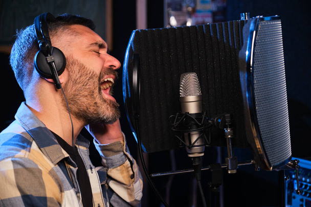 Male vocal artist, singer, with headphones recording new album at a recording studio. - Zdjęcie, obraz