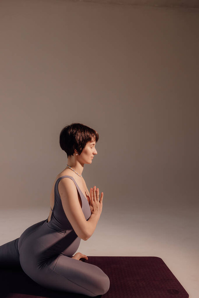 Mujer embarazada joven haciendo ejercicios de yoga y meditando en el estudio. Atención médica, mindfulness, relajación y concepto de bienestar. - Foto, imagen