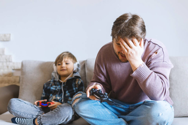 Vater und Sohn sitzen auf Sofa in Lounge und spielen Videospiel.  - Foto, Bild