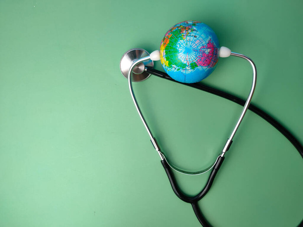 Stethoscoop en aardbol op een groene achtergrond. Gezondheidszorg en medisch concept. - Foto, afbeelding