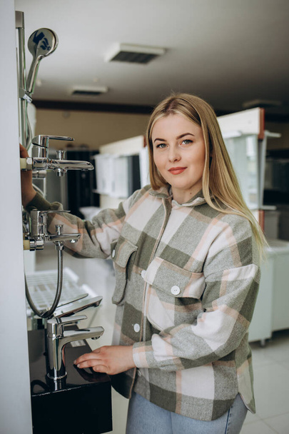 Smiling woman inspects and chooses new kitchen or bath tap faucet at a hardware store - Photo, Image