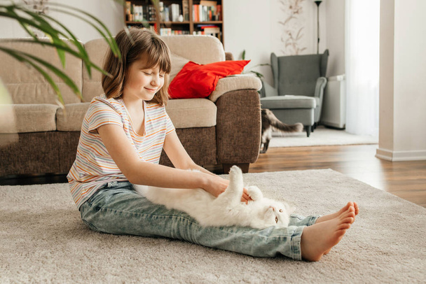 Egy tinédzser lány játszik a szeretett fehér, bolyhos cicájával. A gyerek megcsókolja a macskát. Háziállatok iránti szeretet és gondoskodás. Háziállatok élete a lakásban. - Fotó, kép