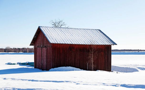 a small red barn in a sunny winter landscape - Φωτογραφία, εικόνα